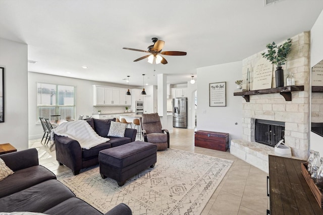 living room featuring ceiling fan, a stone fireplace, and light tile patterned floors