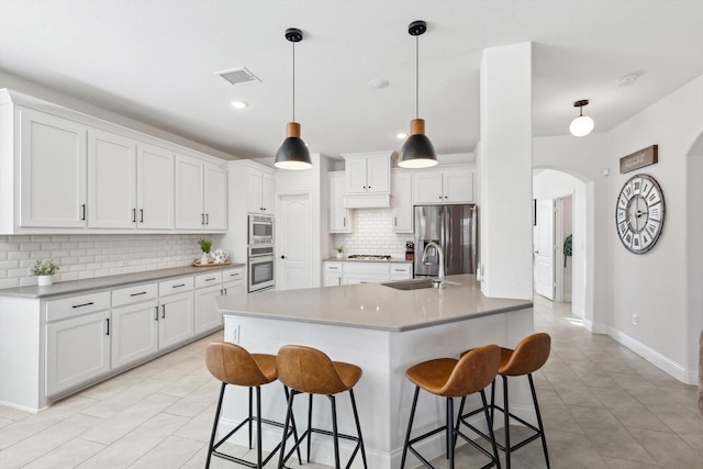 kitchen with stainless steel appliances, pendant lighting, white cabinets, backsplash, and sink