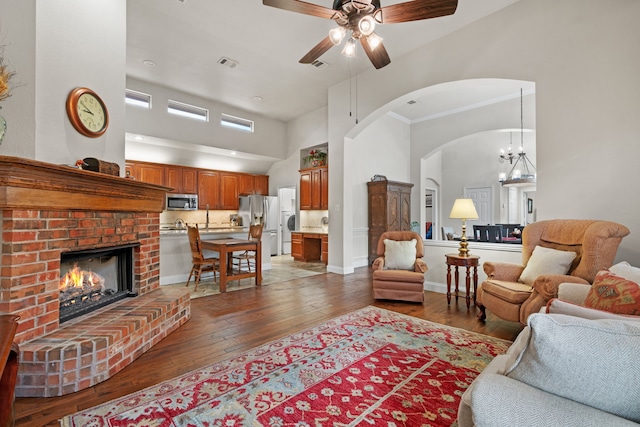 living room featuring hardwood / wood-style flooring, a high ceiling, a fireplace, crown molding, and ceiling fan with notable chandelier