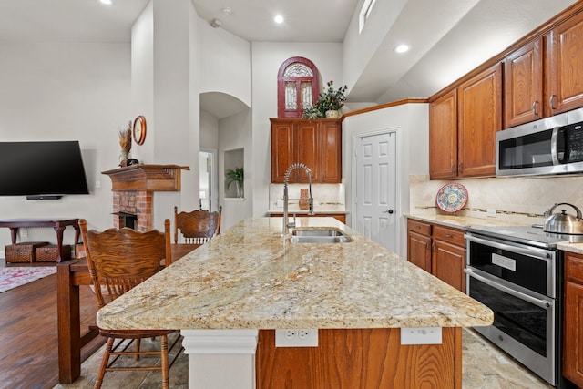 kitchen with a center island with sink, stainless steel appliances, a high ceiling, tasteful backsplash, and sink