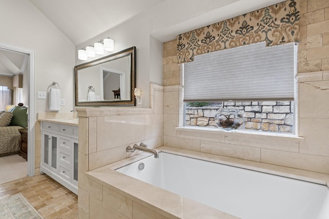 bathroom featuring lofted ceiling, vanity, and a relaxing tiled tub