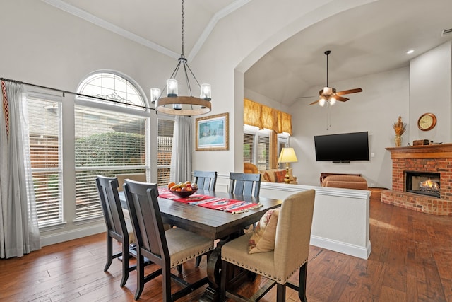 dining area featuring dark hardwood / wood-style floors, lofted ceiling, a fireplace, crown molding, and ceiling fan with notable chandelier