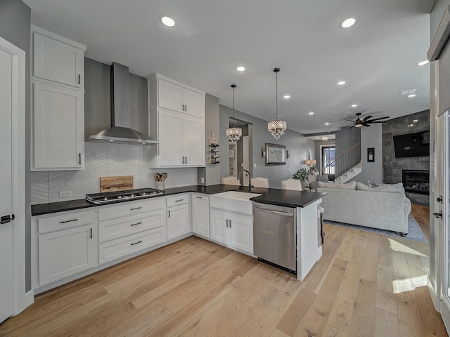 kitchen with appliances with stainless steel finishes, pendant lighting, wall chimney range hood, and white cabinets