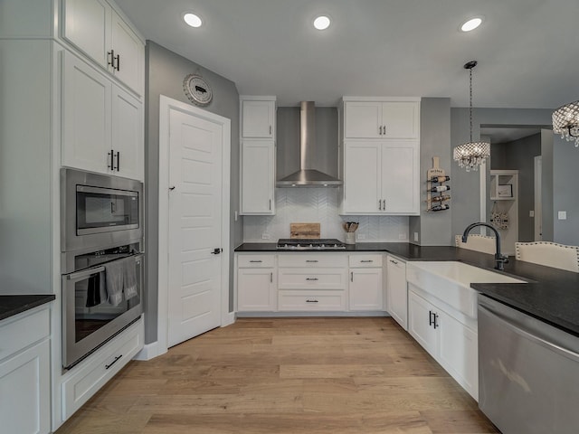 kitchen with white cabinets, stainless steel appliances, pendant lighting, sink, and wall chimney range hood