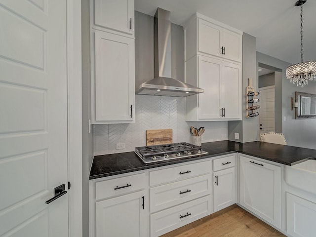 kitchen featuring wall chimney range hood, pendant lighting, and white cabinetry