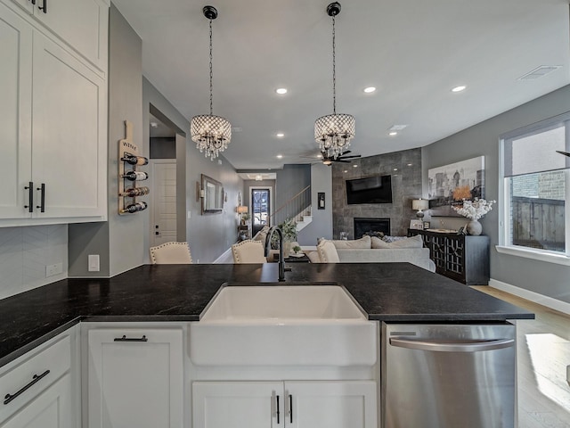 kitchen featuring dishwasher, a tiled fireplace, hanging light fixtures, sink, and white cabinetry