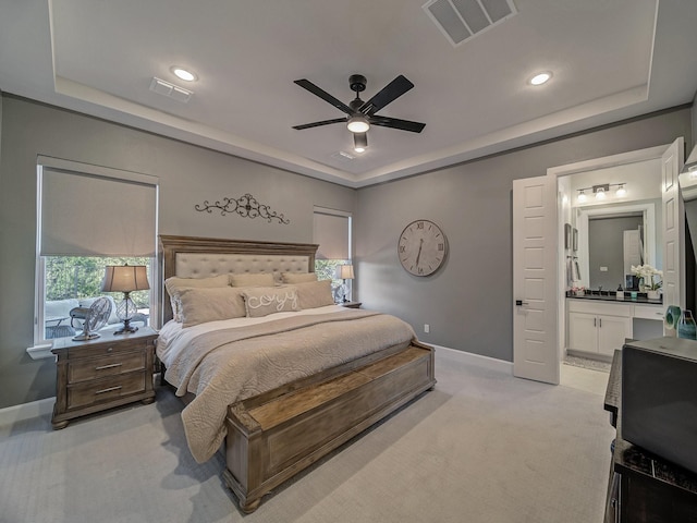 bedroom with ceiling fan, light colored carpet, connected bathroom, and a raised ceiling