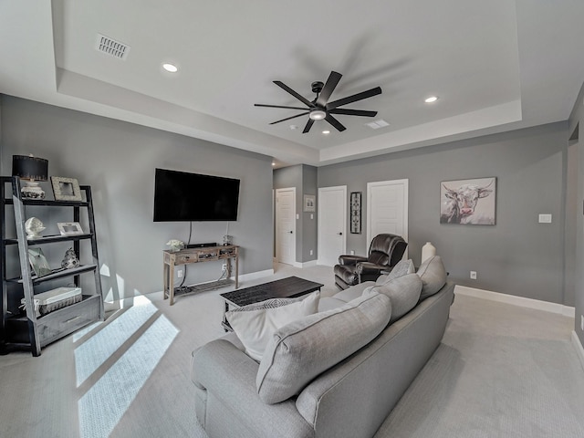 living room featuring a raised ceiling, light carpet, and ceiling fan