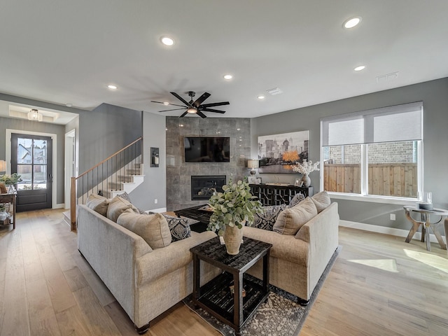 living room with a tiled fireplace, ceiling fan, and light hardwood / wood-style flooring