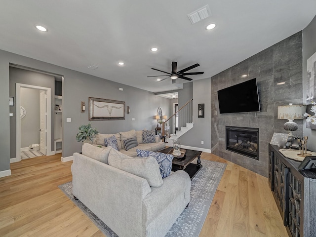 living room with a tile fireplace, light wood-type flooring, and ceiling fan