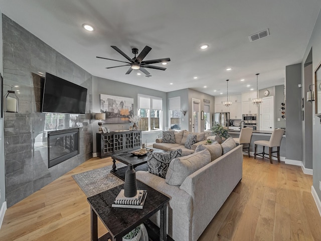 living room with ceiling fan with notable chandelier, a fireplace, and light wood-type flooring