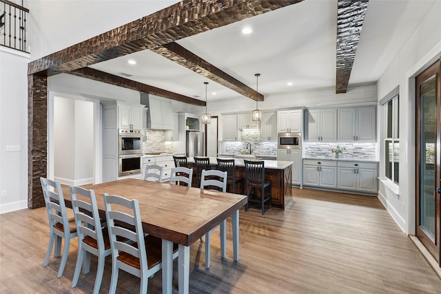 dining room with sink, light hardwood / wood-style floors, and beamed ceiling