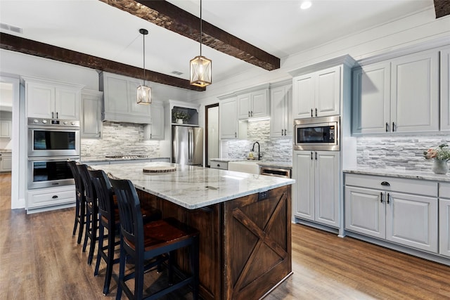 kitchen with stainless steel appliances, light stone countertops, beamed ceiling, and a center island