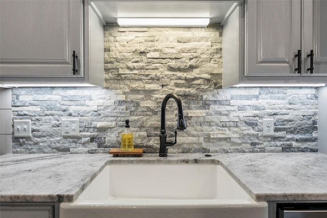 kitchen with sink, tasteful backsplash, light stone counters, and gray cabinets