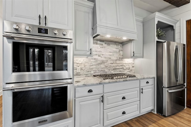 kitchen with stainless steel appliances, white cabinetry, light stone counters, light wood-type flooring, and decorative backsplash