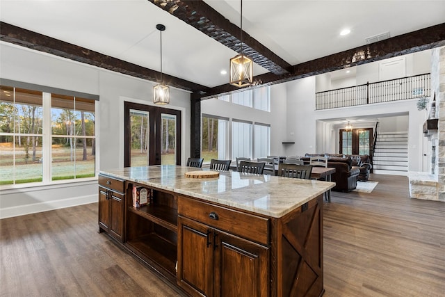 kitchen with light stone countertops, pendant lighting, french doors, dark wood-type flooring, and a kitchen island