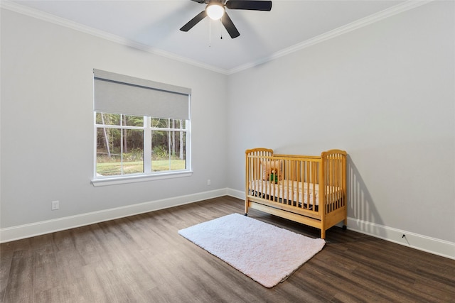 unfurnished bedroom with dark hardwood / wood-style flooring, a nursery area, ceiling fan, and crown molding