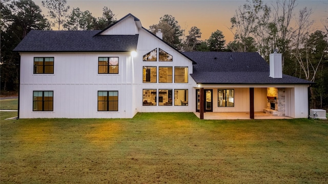 back house at dusk with a patio area and a lawn