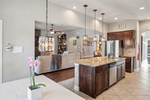 kitchen featuring a kitchen island with sink, stainless steel appliances, hanging light fixtures, sink, and tasteful backsplash