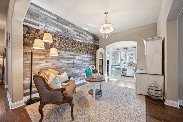 sitting room with dark hardwood / wood-style flooring, wooden walls, and a chandelier