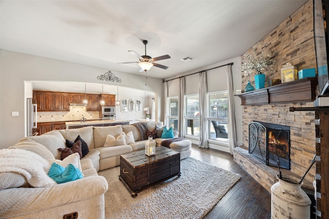 living room with ceiling fan, wood-type flooring, and a stone fireplace