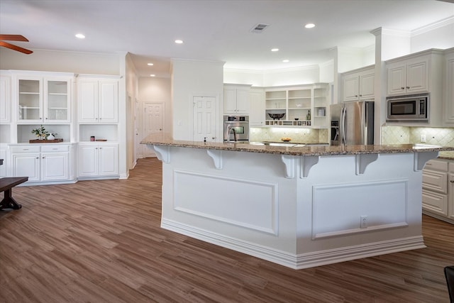 kitchen featuring appliances with stainless steel finishes, stone countertops, a large island with sink, and a breakfast bar area