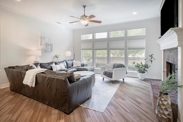 living room featuring a brick fireplace, ornamental molding, a wealth of natural light, and light hardwood / wood-style flooring