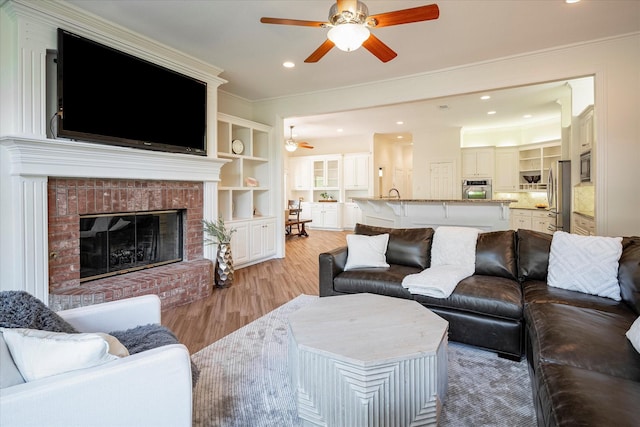 living room with light hardwood / wood-style floors, a brick fireplace, crown molding, and built in shelves