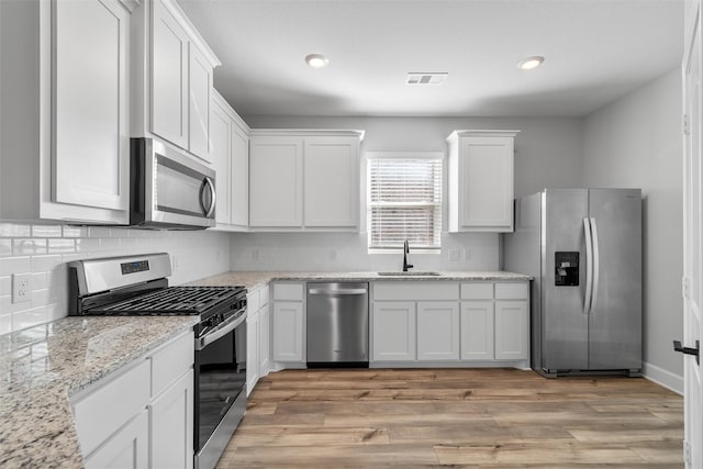 kitchen with light stone counters, light hardwood / wood-style flooring, stainless steel appliances, white cabinets, and sink