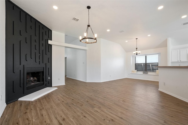 unfurnished living room featuring vaulted ceiling, hardwood / wood-style floors, a large fireplace, and a notable chandelier