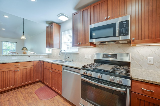 kitchen featuring stainless steel appliances, hanging light fixtures, light stone counters, sink, and light hardwood / wood-style flooring