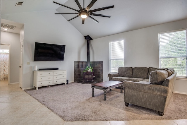 living room featuring vaulted ceiling, ceiling fan, a wood stove, and light tile patterned floors