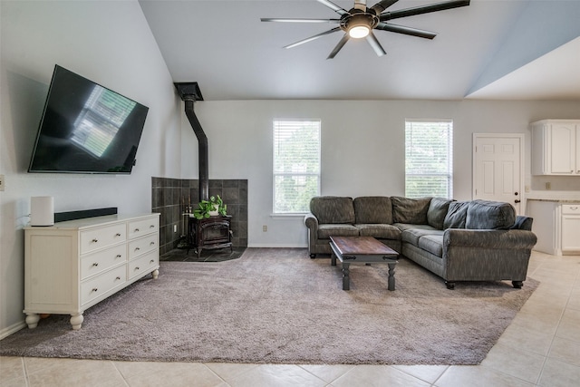 living room with vaulted ceiling, light tile patterned flooring, ceiling fan, and a wood stove