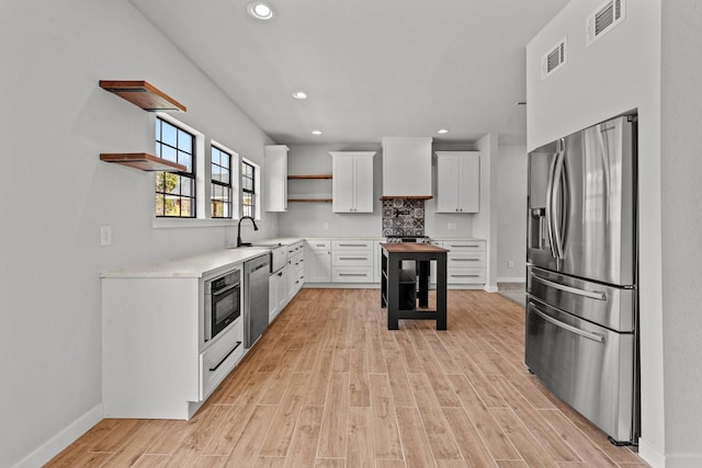 kitchen with open shelves, appliances with stainless steel finishes, white cabinetry, and light wood-style floors