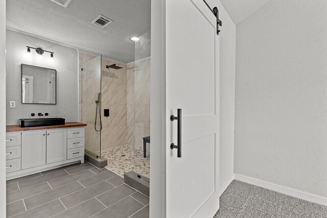 full bathroom featuring visible vents, a tile shower, vanity, a textured ceiling, and baseboards