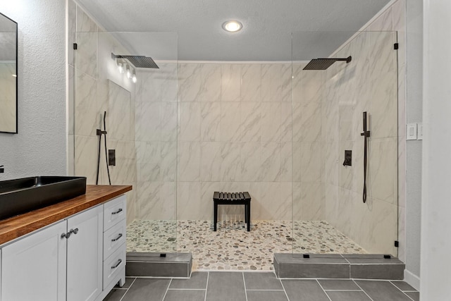 bathroom featuring a textured wall, vanity, a textured ceiling, a walk in shower, and tile patterned floors