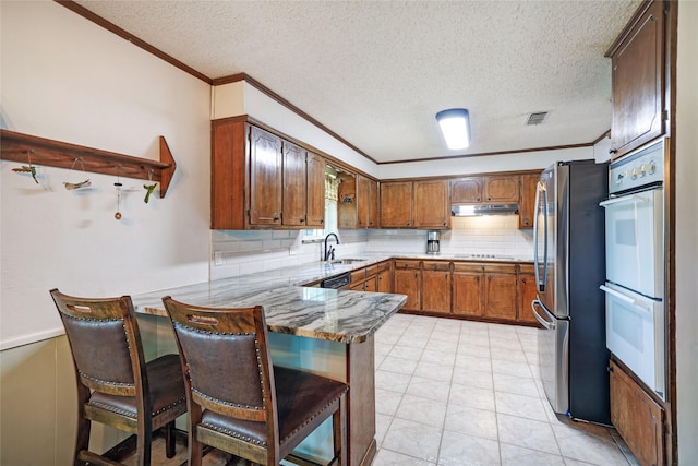 kitchen featuring kitchen peninsula, stainless steel refrigerator, a breakfast bar area, double oven, and sink