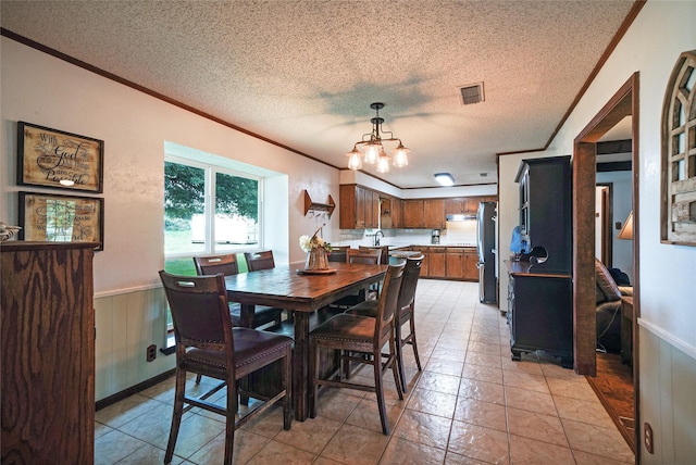 tiled dining room featuring ornamental molding, a notable chandelier, wooden walls, and a textured ceiling