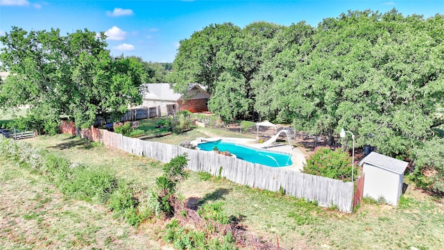 view of swimming pool with a lawn, a water slide, and a storage shed