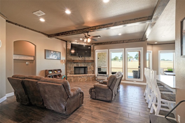 living room featuring a textured ceiling, ceiling fan, and a stone fireplace