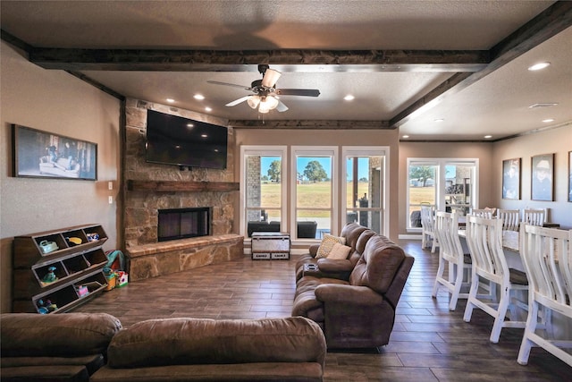 living room with a textured ceiling, ceiling fan, and a stone fireplace