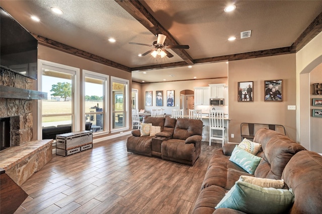 living room featuring a textured ceiling, ceiling fan, beamed ceiling, and a fireplace