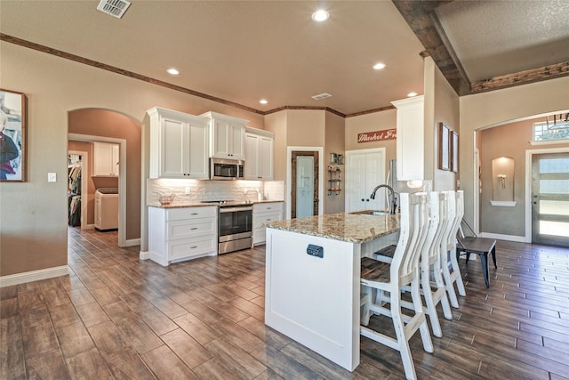 kitchen with kitchen peninsula, stainless steel appliances, light stone countertops, and white cabinetry