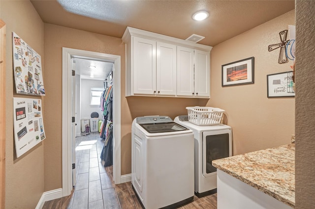 laundry room with washer and dryer, a textured ceiling, and cabinets