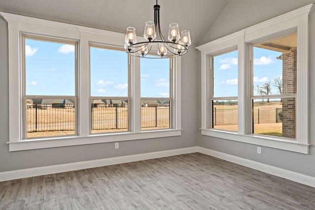 interior space with a notable chandelier, vaulted ceiling, hardwood / wood-style floors, and plenty of natural light