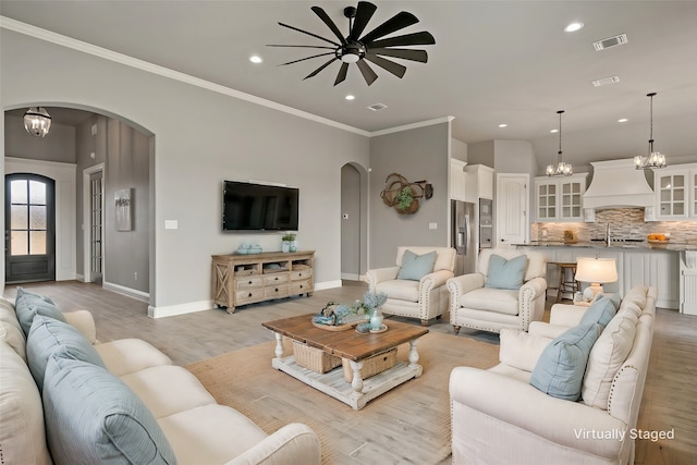 living room with crown molding, sink, light hardwood / wood-style floors, and ceiling fan with notable chandelier