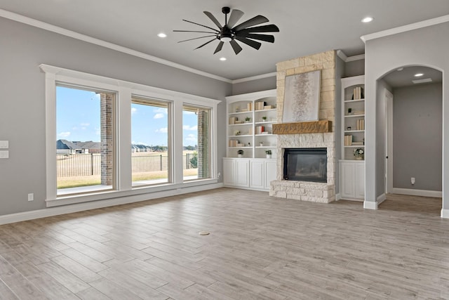 unfurnished living room with built in shelves, ornamental molding, ceiling fan, a fireplace, and light hardwood / wood-style floors