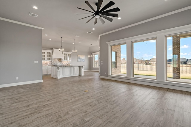 unfurnished living room featuring ornamental molding, sink, wood-type flooring, and ceiling fan with notable chandelier