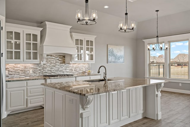 kitchen featuring lofted ceiling, sink, premium range hood, white cabinetry, and a center island with sink