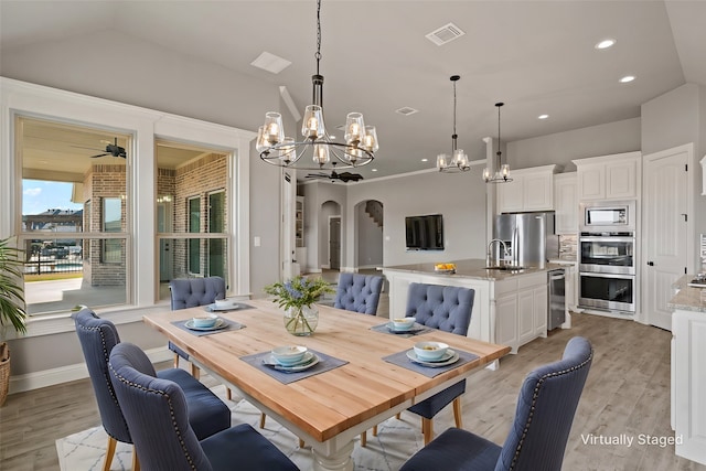 dining space featuring sink, ceiling fan with notable chandelier, light hardwood / wood-style flooring, and vaulted ceiling